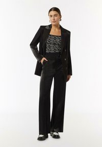 Black tailored blazer with satin finish, black and white patterned bodysuit, wide-leg black trousers, and black shoes with white accents.
