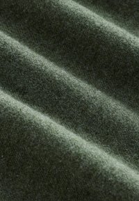 Tessuto di lana verde con una superficie morbida e testurizzata, caratterizzato da pieghe visibili e un colore uniforme. Ideale per abbigliamento o tappezzeria.