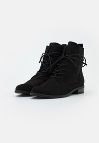 Bottes chevilles en daim noir avec un bout arrondi, un avant à lacets et un petit talon carré. Texture lisse avec des détails de couture subtils.