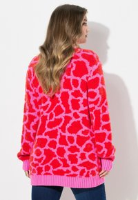 Jasně červený, nadýchaný svetr s růžovým abstraktním vzorem. Má růžové žebrované manžety a lem, volný oversized střih a jemnou strukturu.