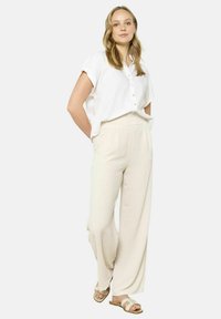 Lightweight white button-up shirt, relaxed fit. Soft, flowing beige wide-leg pants. Casual sandals with a padded strap.