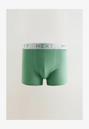 Žalios medvilninės kelnaitės su baltu juosmeniu, kuriame užrašyta "NEXT" žaliais rašmenimis, sukurtos su plokščiomis siūlėmis ir prigludusiu pavidalu.