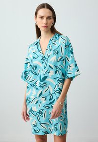 Abito a manica corta con sfondo turchese e motivo floreale in teal, bianco e crema. Scollatura a V e vestibilità ampia.