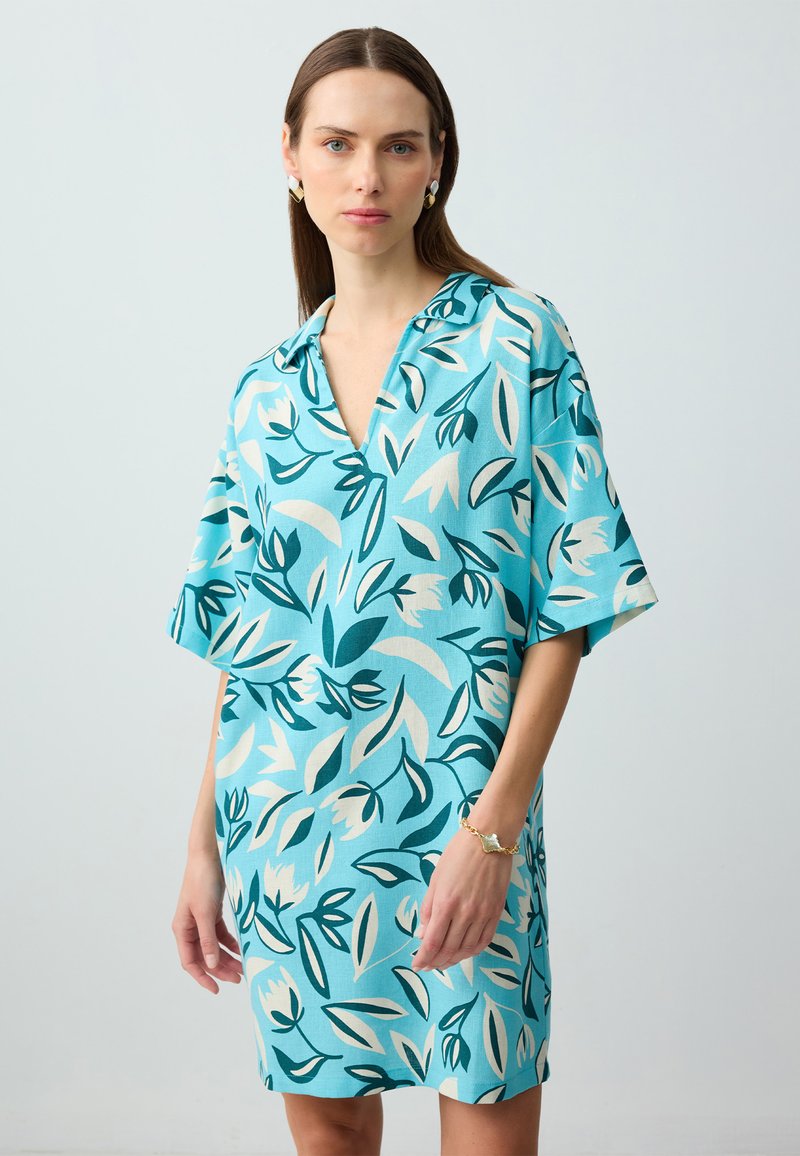 Abito a manica corta con sfondo turchese e motivo floreale in teal, bianco e crema. Scollatura a V e vestibilità ampia.