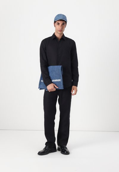Chemise noire à boutons, pantalon foncé, sac en denim avec le logo "SAMSOE", casquette bleu clair et chaussures noires. Style simple, coupe ajustée avec des lignes épurées.
