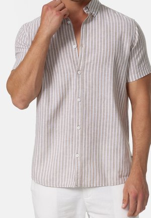 Man wearing short-sleeve beige and white vertical striped button-up shirt with white pants, hand near collar adjusting shirt.