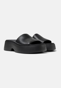 Sandales en cuir noir à semelle plate, avec une large ouverture à l'avant. Elles présentent une semelle épaisse et texturée ainsi qu'un dessus lisse. Aucun embellissement supplémentaire.