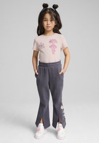 Lyserød t-shirt med grafisk design, parret med mørkegrå sweatpants med sideskår og blomsterdetaljer. Hvide sneakers med lyserøde detaljer.