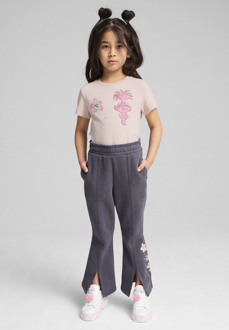 Lyserød t-shirt med grafisk design, parret med mørkegrå sweatpants med sideskår og blomsterdetaljer. Hvide sneakers med lyserøde detaljer.