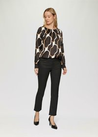 Schwarze und cremefarbene Langarmbluse mit abstraktem Muster, kombiniert mit schwarzen, eng anliegenden Hosen und schwarzen spitzen High Heels. Glatte Stoffstruktur.