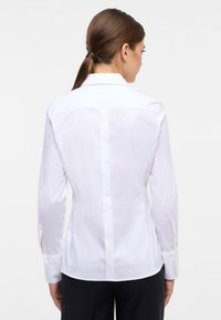 Witte, lang-sleeve shirt met een puntige kraag, getailleerde pasvorm en knoopmanschetten. Soepele textuur en subtiele nadenafwerking aan de achterkant.