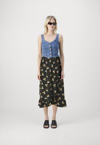 Gombokkal ellátott farmer crop top, fekete virágmintás midi szoknyával, fodros szegéllyel párosítva. A szettet egy pár fekete papucs egészíti ki.