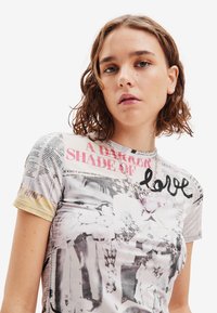 Camiseta gráfica con diseño de papel periódico en blanco y negro, acentuada por elementos coloridos y la palabra "amor" en una escritura en negrita. Manga corta.