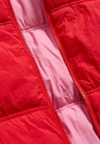 Rode pufferjack met een roze binnenvoering, voorzien van een volledige rits met een contrasterende rode ritsband en gathered elastische naden voor textuur.
