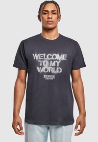 Juodas medvilninis marškinėliai su balta purkštuko spausdinimo užrašu "WELCOME TO MY WORLD" ir "STRANGER THINGS" logotipu apačioje. Trumpomis rankovėmis, apvalia iškirpte.