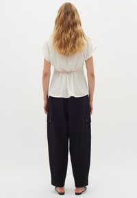 Top bianco a maniche corte con vita arricciata, abbinato a pantaloni neri larghi con tasche laterali e una texture liscia.