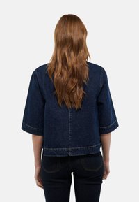 Veste en denim bleu foncé avec des manches larges, un design court et des détails de couture visibles. Dispose d'une couture arrière droite et d'un matériel minimal.