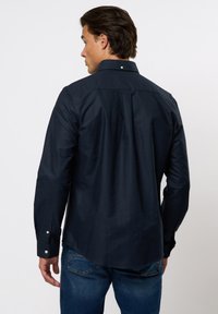 Navy Hemd aus Baumwolle mit langen Ärmeln, Kentkragen und abgerundetem Saum. Verfügt über weiße Knöpfe und eine glatte Textur.
