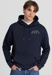 Felpa con cappuccio di colore blu navy, dotata di una tasca frontale e decorata con la scritta bianca "NORTH CAROLINA" su un tessuto morbido e testurizzato.