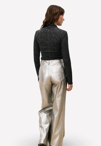 Zwarte doorschijnende top met lange mouwen, gecombineerd met metallic zilveren broek met hoge taille en wijde pijpen. Opvallende achterzakken aan de broek.