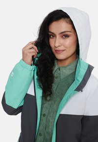 Daugiaspalvė lengva striukė mėtų žalios, baltos ir tamsiai pilkos spalvos, su kapuce; turi pilną užtrauktuką ir elastingus rankogalius.