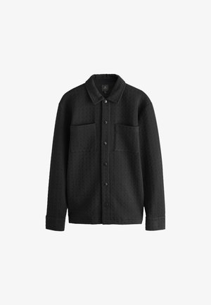 Czarna pikowana kurtka koszulowa z kołnierzykiem, przednim zapięciem na guziki i dwoma kieszeniami na piersi. Teksturowana tkanina z wzorem w kratę.