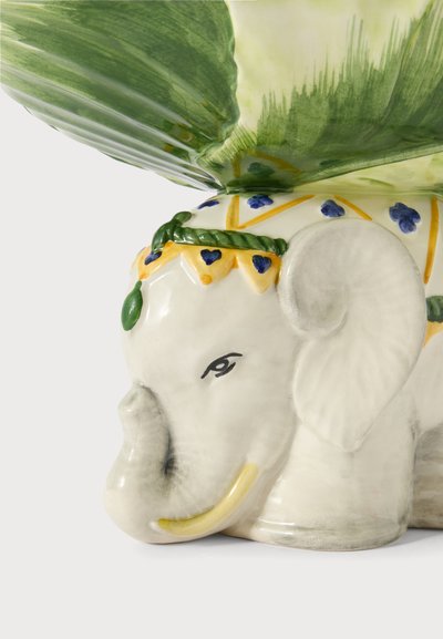 Cache-pot éléphant en céramique avec un ornement de tête décoratif peint, tenant de grandes feuilles vertes qui s'étendent vers le haut.