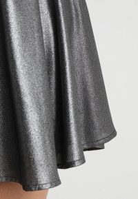 Jupe métallique noire avec une surface brillante, design évasé et texture douce, présentant un ourlet qui se courbe doucement sur les bords.