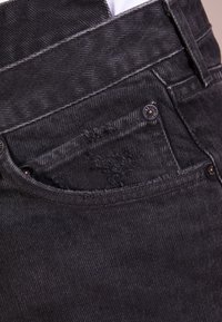 Jeans in denim nero con una finitura testurizzata, passanti per cintura, una tasca frontale con bordi sfilacciati e elementi in metallo decorativi.