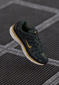 Nike sneakers in dark green with yellow accents, featuring a textured upper, cushioned sole, and laces. Lightweight and breathable design.