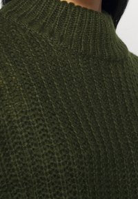 Pletený svetr v tmavě zelené barvě s texturovaným, žebrovan�ým vzorem a vysokým límcem. Materiál se zdá být měkký a mírně chlupatý.