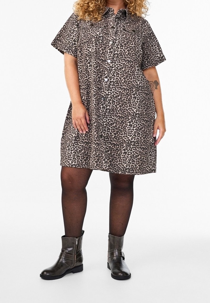 Femme portant une robe à manches courtes avec fermeture à boutons à l’avant, imprimé léopard, collants noirs et bottines foncées sur fond blanc.