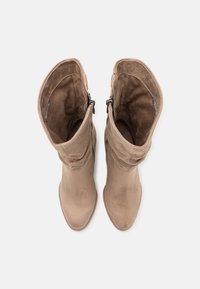 Beige suède knähöga stövlar med en slouchy design och en jämn yta. Har en dragkedja på utsidan för enkel påtagning.