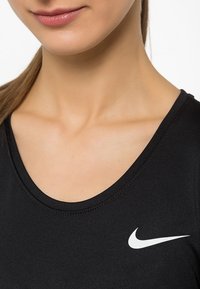 Musta urheilu paita, jossa on pyöreä pääntie. Vasemmalla puolella pieni valkoinen Nike-logo. Sileä pinta.