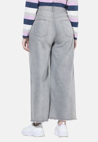 Široké šedé džíny s vysokým pasem, s zadními kapsami a roztrhaným lemem, zkombinované s bílými teniskami.