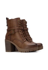 Botas de piel marrón hasta el tobillo con un tacón grueso, que presentan ojales de metal, detalles de hebilla y una suela texturizada para un mejor agarre.