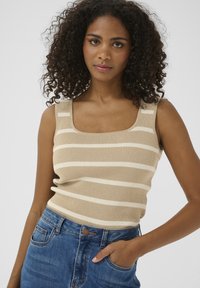 Débardeur beige à côtes avec des rayures blanches horizontales. Présente un décolleté carré et des bretelles larges, associé à un jean en denim bleu.