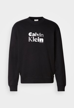Melns kokvilnas kapucis ar ribotu apkakli un piedurknēm. Ar baltu izdrukātu logotipu, kas lasa "Calvin Klein." Gluda tekstūra.