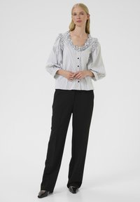 Striped button-up blouse with ruffled neckline and long sleeves, paired with black tailored pants and pointed black shoes.