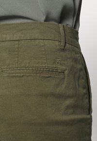 Pantalon vert olive à texture lisse, doté d'une poche arrière plaquée et de détails de couture subtils, conçu avec une coupe droite.