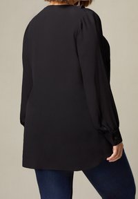 Svart långärmad blus med en slät textur, rund halsringning och knäppta manschetter. Baksidan har en rundad fåll för en avslappnad passform.