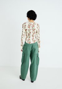 Cremefarvet, ribbet langærmet top med blomsterprint og rygknapper, parret med løstsiddende, grønne cargo-bukser med sidelommer og elastiske manchetter.