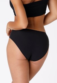 Slip bikini nero a vita alta realizzato in tessuto morbido con un design aderente, caratterizzato da cuciture discrete e senza ulteriori motivi o accenti.
