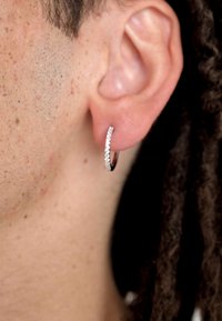 Huggie-hoop oorbel gemaakt van zilverkleurig metaal, met een rij kleine heldere edelstenen die langs de voorkant zijn gezet, en een strak ontwerp.