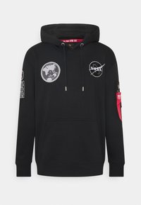 Sudadera negra con bolsillo tipo canguro, cordones y múltiples parches del logo de la NASA. Presenta un bolsillo con cremallera en la manga con un acento rojo.