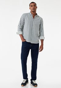 Gestreept overhemd in blauw en wit, gecombineerd met donkere jeans en marineblauwe sneakers. Het shirt heeft opgerolde mouwen en een ontspannen pasvorm.