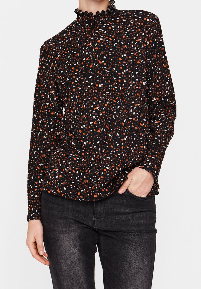 Blusa nera con colletto alto arricciato, caratterizzata da un motivo sparso in arancione, bianco e blu su un tessuto testurizzato. Maniche lunghe visibili.