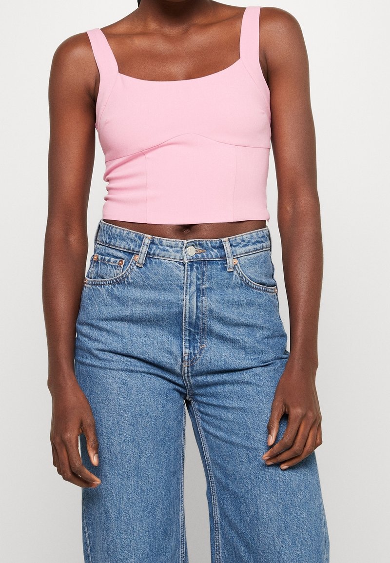 Lyserød cropped tanktop med firkantet halsudskæring, strækstof og brede stropper, parret med lyseblå højtaljede jeans.