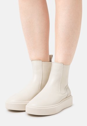Ankle-high cream leather platform boots with rounded toes worn on bare legs, shown against a plain light background.