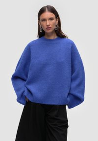 Königsblaues, übergroßes Sweatshirt mit rundem Ausschnitt, lockeren Ärmeln und einem weichen, strukturierten Stoff, kombiniert mit dunklen Hosen.